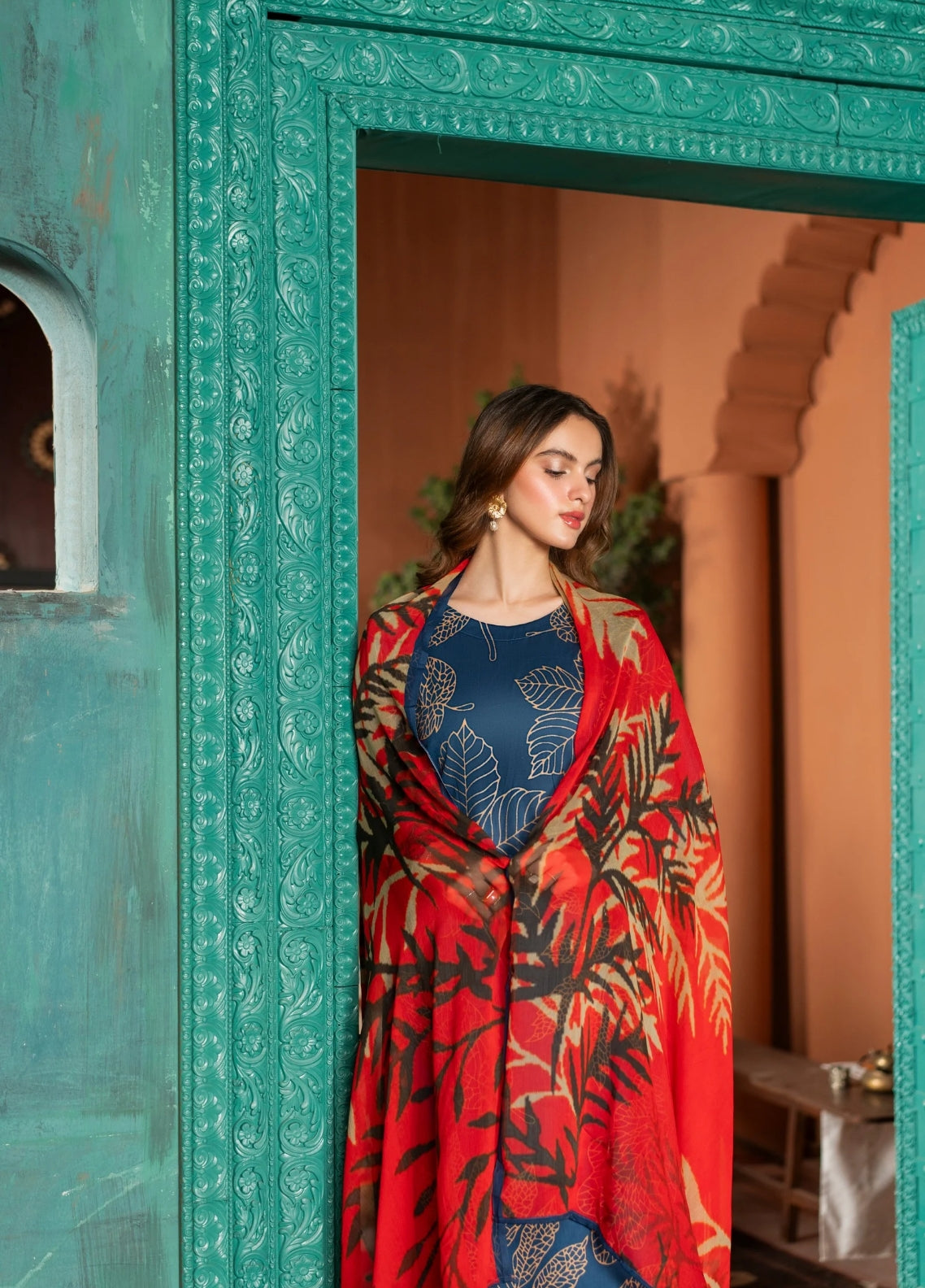 A woman wearing a lawn digital printed blue and red dress with chiffon dupatta, standing against a turquoise background.